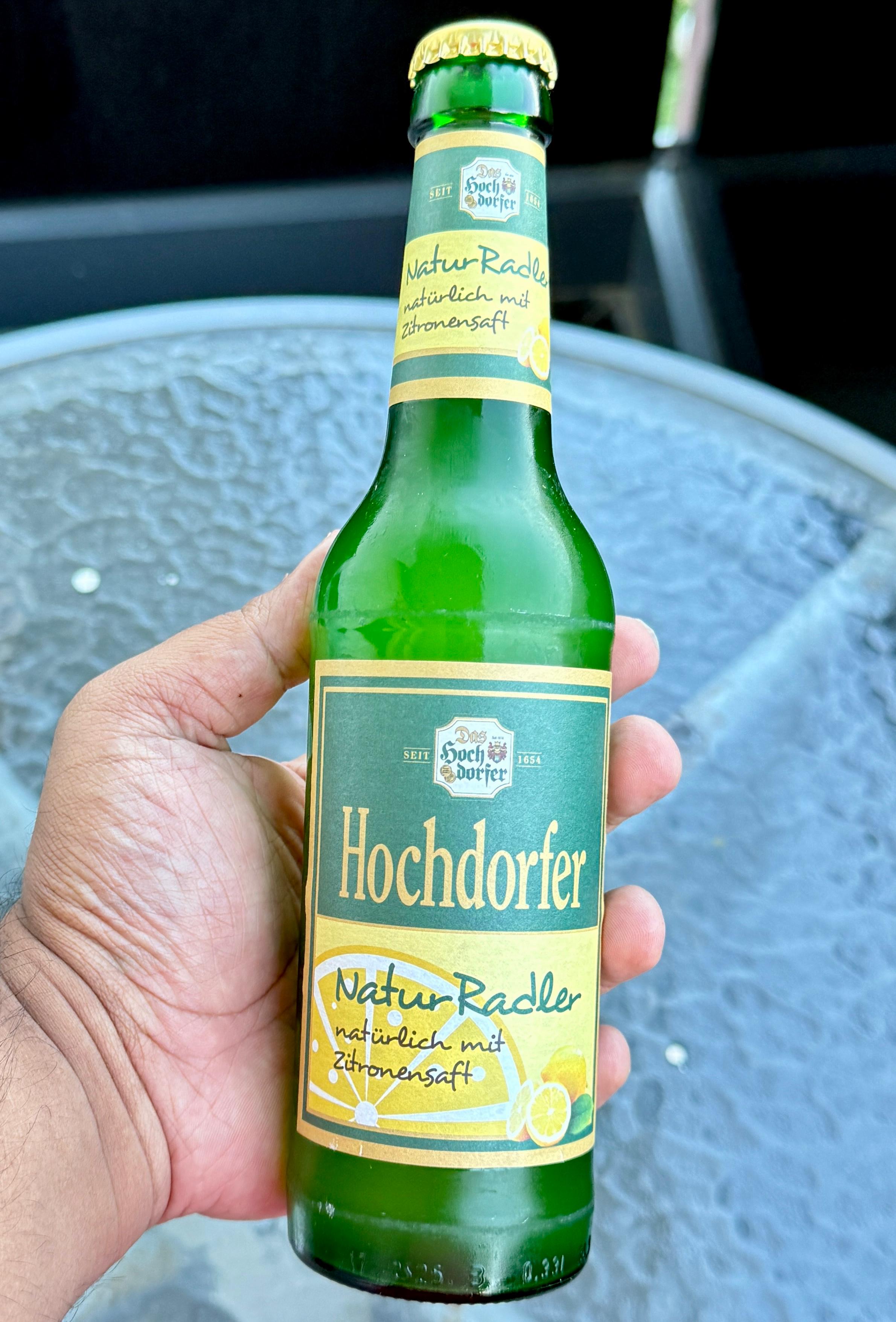 A hand holding a green bottle of Hochdorfer NaturRadler